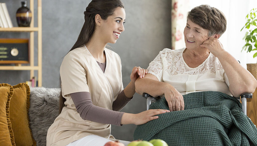 A Young Volunteering Caregiver Sitting Beside a Smiling Elderly Woman in a Wheelchair Is Hospice Volunteering Clinical