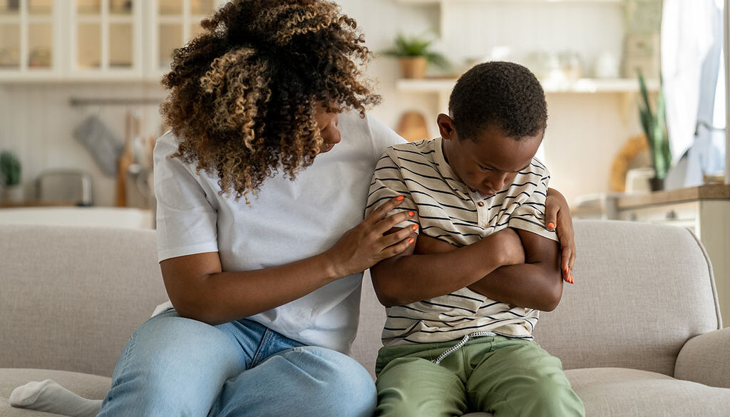 An African American Mother Sitting Beside Her Upset Son on a Couch Hugging Him Grief Counseling for Kids