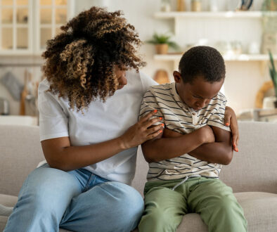 An African American Mother Sitting Beside Her Upset Son on a Couch Hugging Him Grief Counseling for Kids