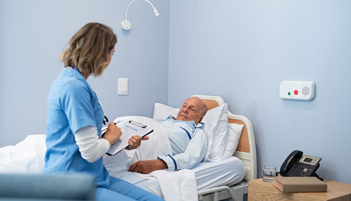 A Nurse Talking With a Senior Patient While Writing on a Clipboard Sitting on the Edge of a Hospital Bed How Long Can You Stay in Inpatient Hospice