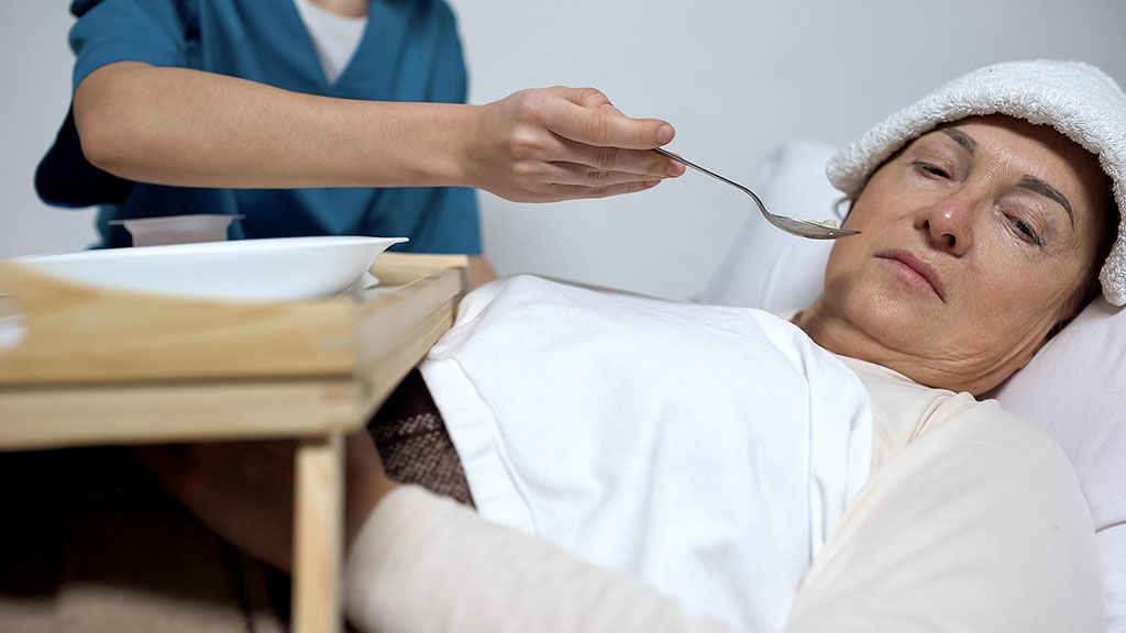 A Terminally Ill Woman Turning Her Face Away From a Spoon of Food Being Served by a Nurse Hospice Patient Not Eating