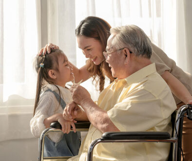 A Senior Man Sitting in a Wheelchair Smiling With His Daughter and Granddaughter Beside Him Benefits of Inpatient Hospice for Families