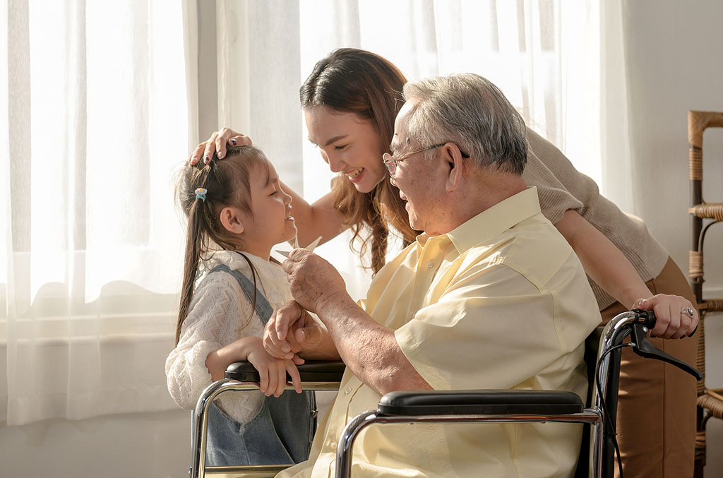 A Senior Man Sitting in a Wheelchair Smiling With His Daughter and Granddaughter Beside Him Benefits of Inpatient Hospice for Families