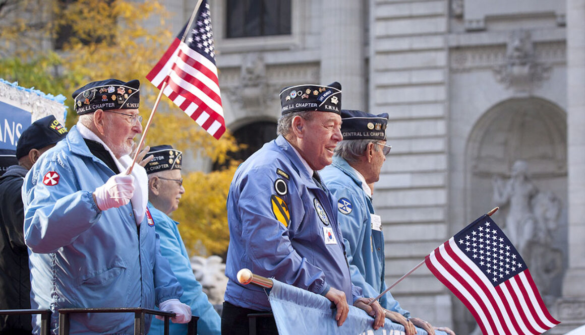 Three Veterans Standing on a Float Holding American Flags During a Parade Veterans in Hospice