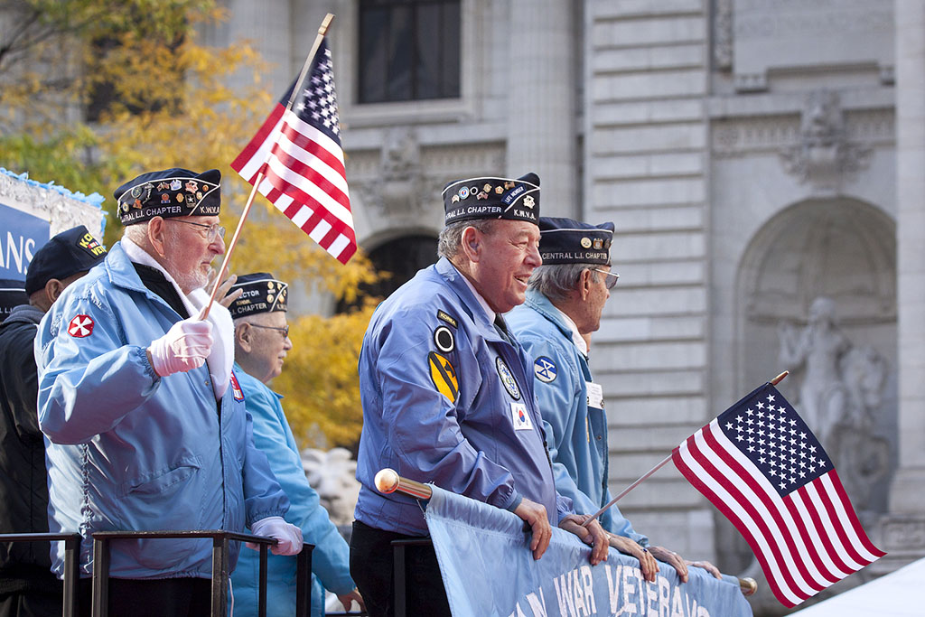 Three Veterans Standing on a Float Holding American Flags During a Parade Veterans in Hospice