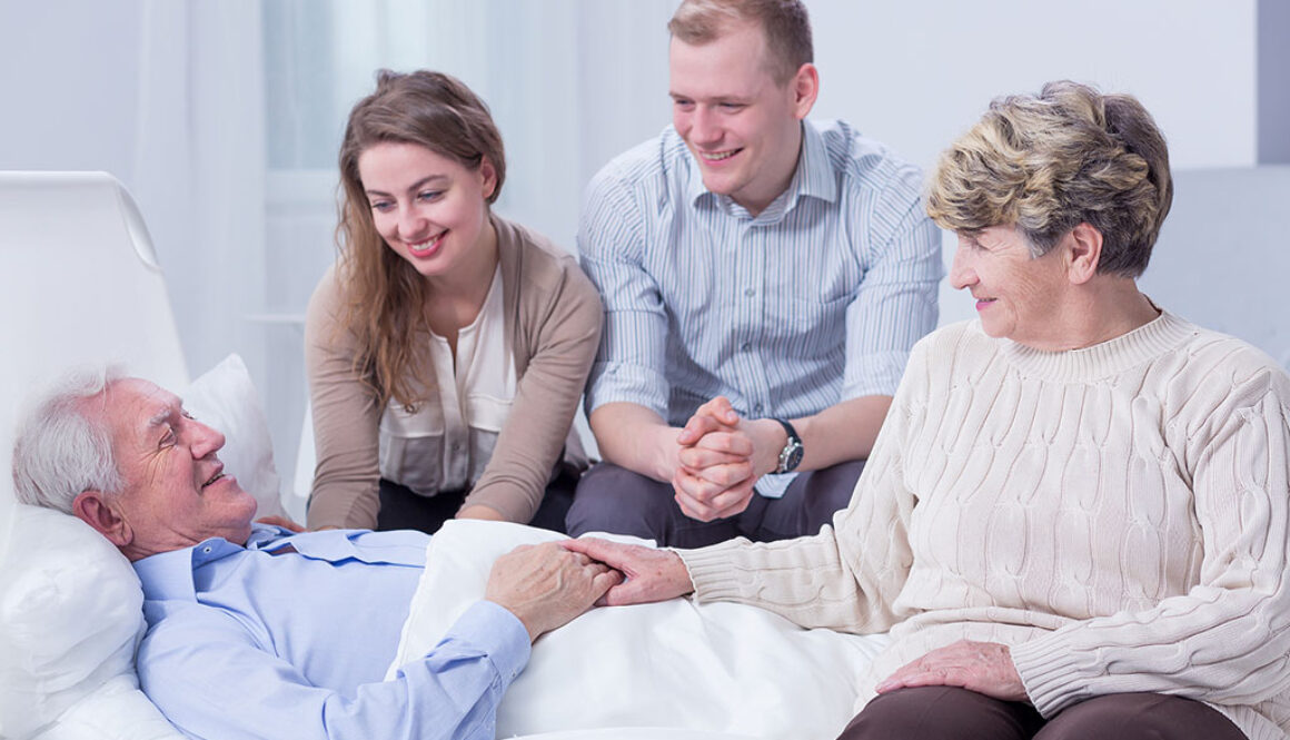 A Senior Man Laying On A Bed Surrounded By His Family In A Hospice Inpatient Unit