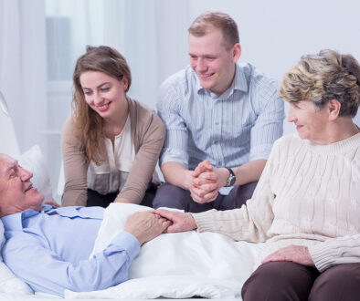 A Senior Man Laying On A Bed Surrounded By His Family In A Hospice Inpatient Unit